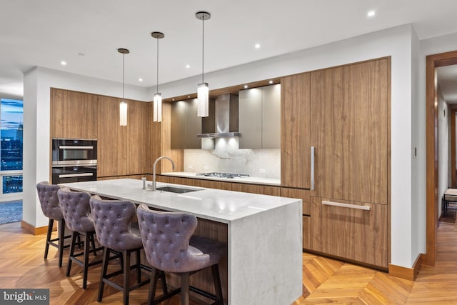 kitchen with sink, wall chimney range hood, gas cooktop, a kitchen breakfast bar, and decorative backsplash