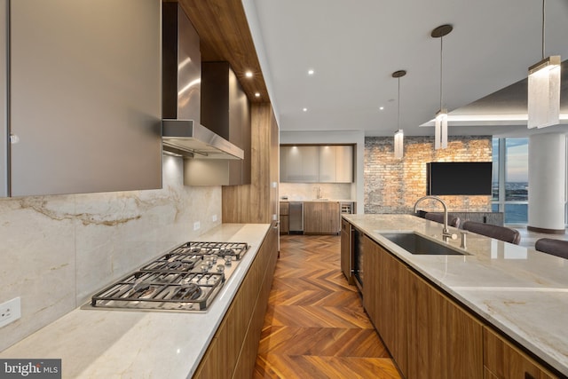 kitchen featuring light stone countertops, sink, wall chimney range hood, dark parquet floors, and decorative light fixtures