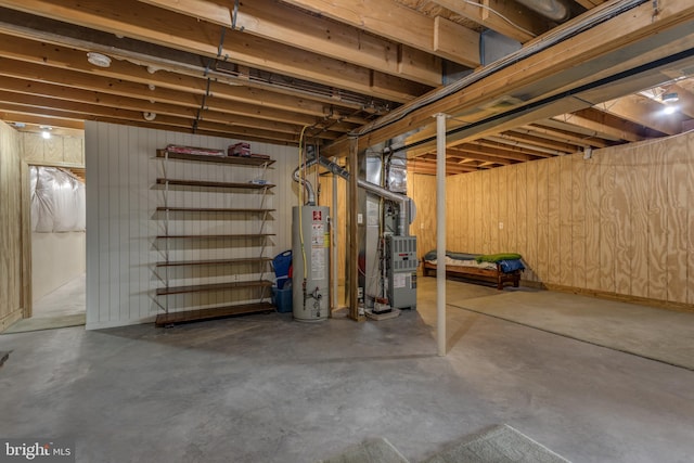 basement featuring heating unit, wooden walls, and water heater