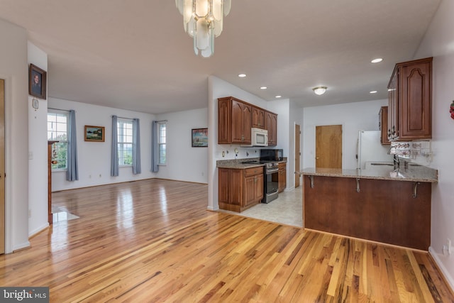 kitchen with sink, white appliances, light hardwood / wood-style floors, kitchen peninsula, and light stone countertops