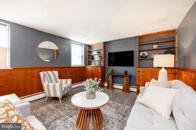 living room with a baseboard radiator, built in features, and wooden walls