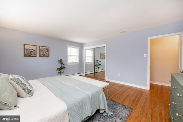 bedroom with hardwood / wood-style floors, a closet, and a baseboard heating unit