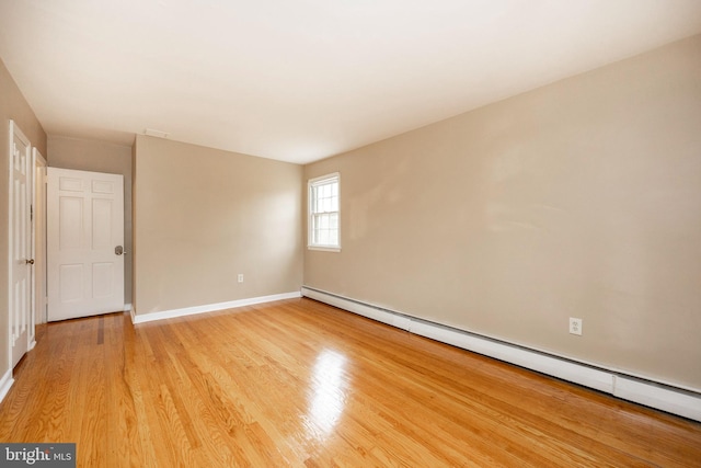 unfurnished room with a baseboard heating unit and light hardwood / wood-style floors