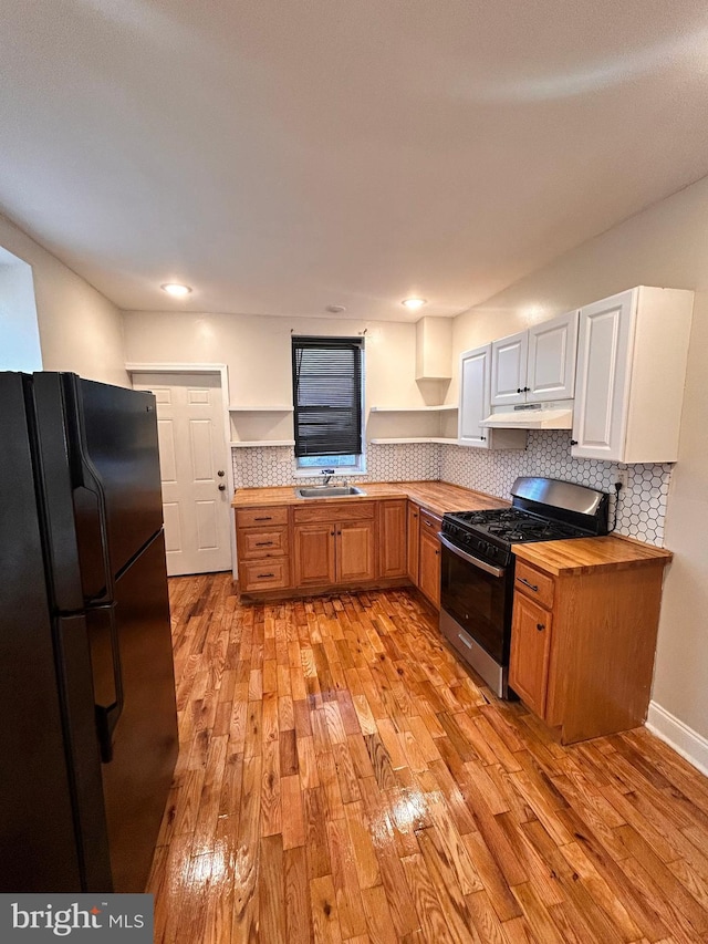 kitchen featuring stainless steel gas stove, sink, light hardwood / wood-style flooring, butcher block countertops, and black refrigerator