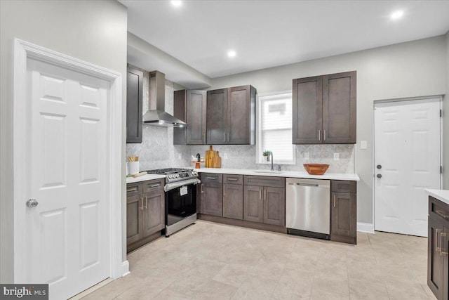 kitchen featuring dark brown cabinets, sink, wall chimney range hood, and appliances with stainless steel finishes