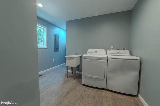 laundry area with electric panel, sink, light hardwood / wood-style floors, and washer and dryer