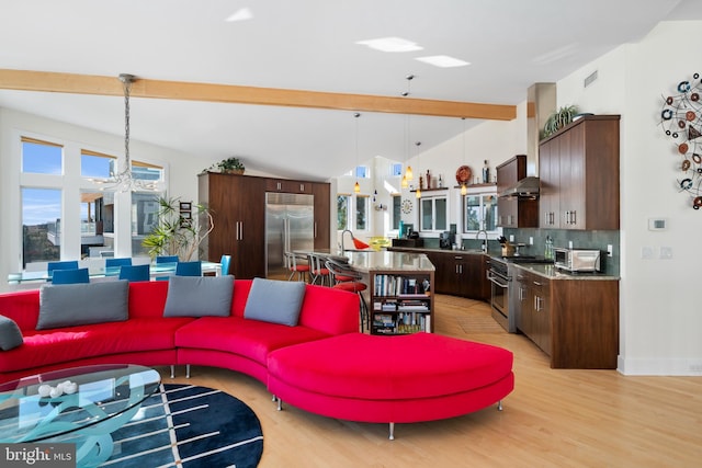 living room with a notable chandelier, lofted ceiling with beams, light hardwood / wood-style floors, and sink