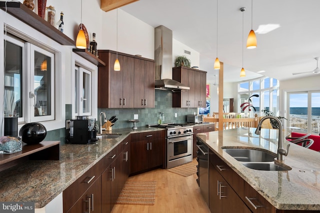 kitchen featuring wall chimney range hood, high end stove, hanging light fixtures, and sink