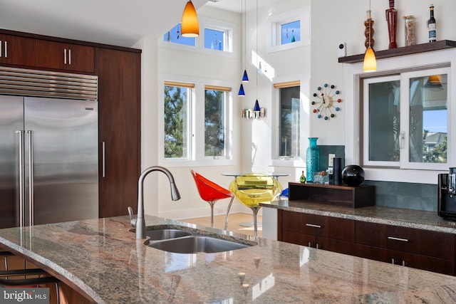 kitchen featuring stone counters, sink, stainless steel built in fridge, decorative light fixtures, and dark brown cabinets