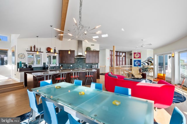 dining room with ceiling fan with notable chandelier, beam ceiling, wood-type flooring, and high vaulted ceiling