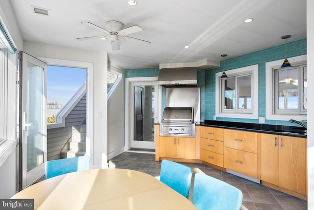 kitchen with wall chimney exhaust hood, ceiling fan, sink, light brown cabinets, and pendant lighting