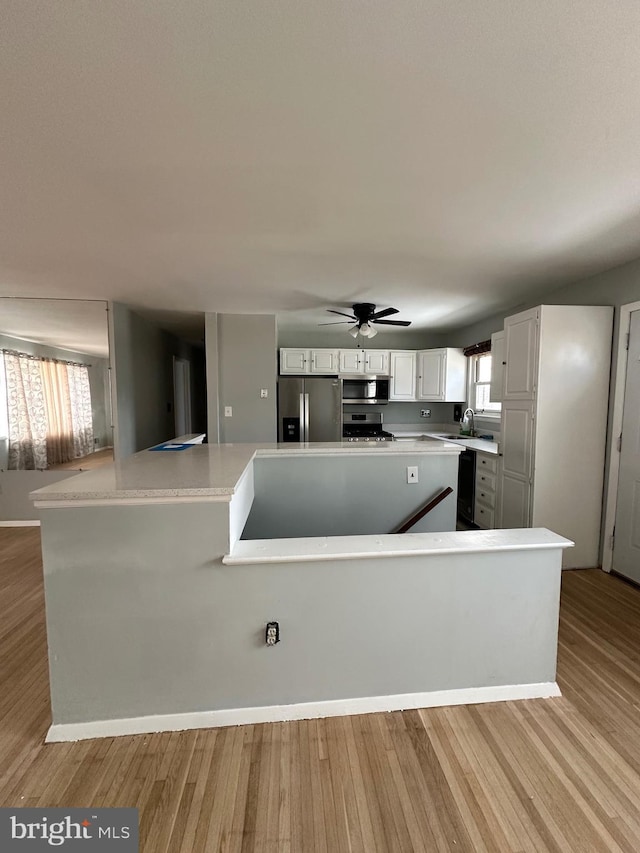 kitchen featuring appliances with stainless steel finishes, kitchen peninsula, light hardwood / wood-style floors, and white cabinets