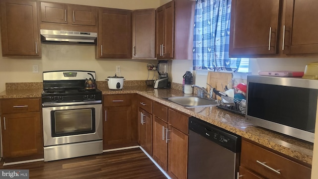 kitchen featuring sink, dark hardwood / wood-style flooring, range hood, dark stone countertops, and appliances with stainless steel finishes