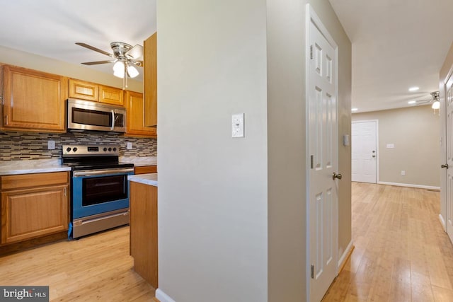 kitchen with ceiling fan, backsplash, appliances with stainless steel finishes, and light hardwood / wood-style flooring