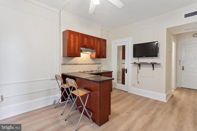 kitchen with ceiling fan, light hardwood / wood-style flooring, backsplash, kitchen peninsula, and a breakfast bar