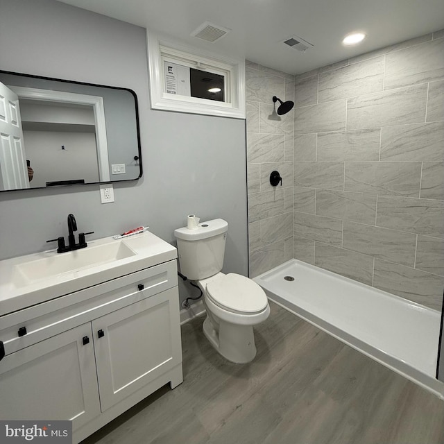 bathroom featuring toilet, a tile shower, vanity, and wood-type flooring