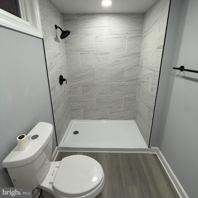 bathroom with toilet, hardwood / wood-style flooring, and tiled shower