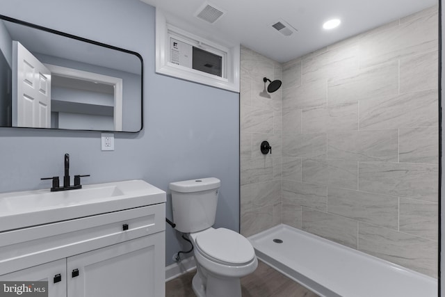 bathroom featuring toilet, wood-type flooring, tiled shower, and vanity