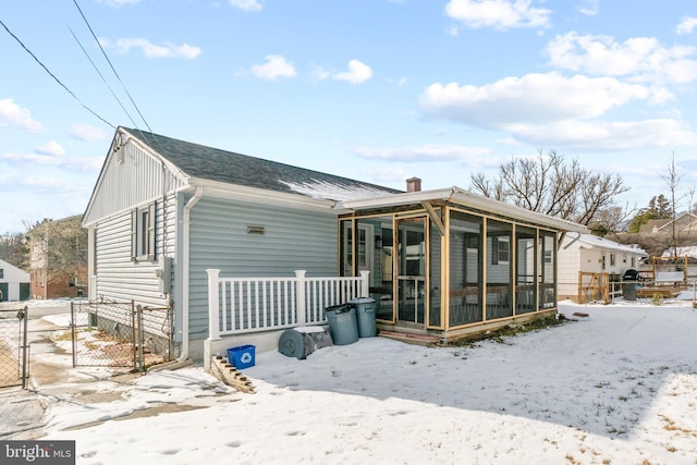 snow covered back of property with a sunroom