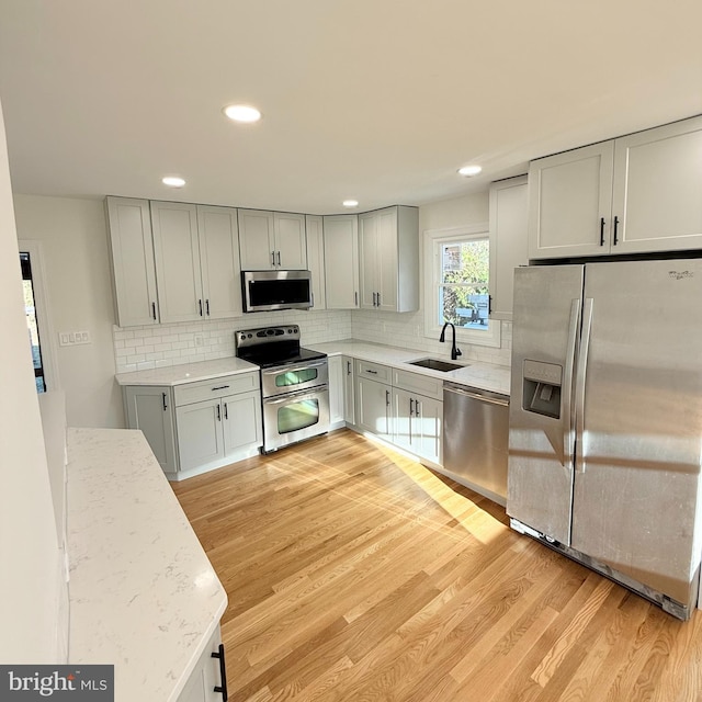 kitchen featuring stainless steel appliances, sink, light hardwood / wood-style floors, backsplash, and gray cabinets