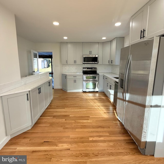 kitchen with light wood-type flooring, backsplash, and appliances with stainless steel finishes