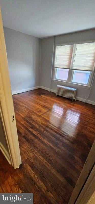 empty room with radiator, dark hardwood / wood-style flooring, and a healthy amount of sunlight