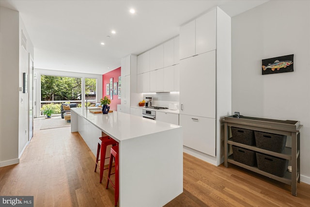 kitchen with a kitchen bar, white cabinetry, a center island, and light hardwood / wood-style floors