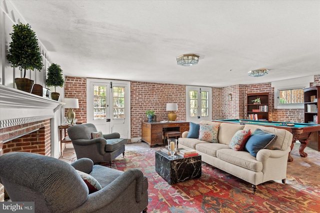 living room featuring a fireplace, a healthy amount of sunlight, brick wall, and billiards