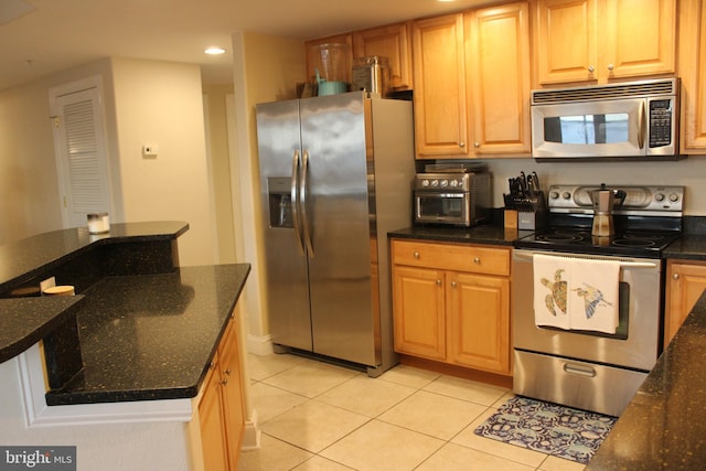 kitchen featuring light tile patterned floors, appliances with stainless steel finishes, and dark stone counters