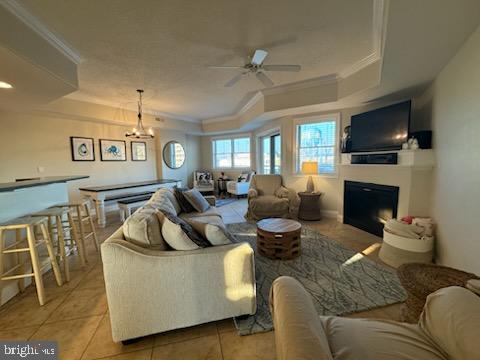 tiled living room featuring a tray ceiling, crown molding, and ceiling fan with notable chandelier