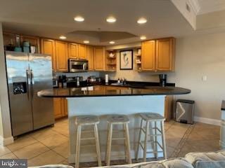 kitchen featuring a kitchen bar, light tile patterned floors, stainless steel appliances, and a tray ceiling