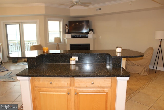 kitchen featuring ceiling fan, a center island, dark stone countertops, crown molding, and light tile patterned floors