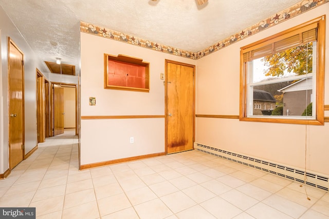 spare room featuring light tile patterned flooring, a baseboard radiator, and a textured ceiling