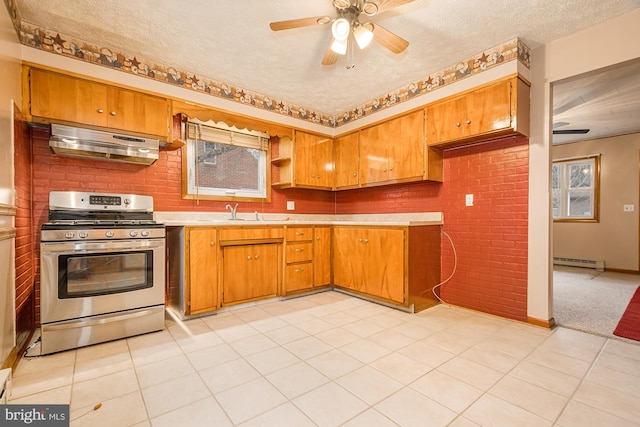 kitchen featuring brick wall, gas range, ceiling fan, a baseboard radiator, and range hood