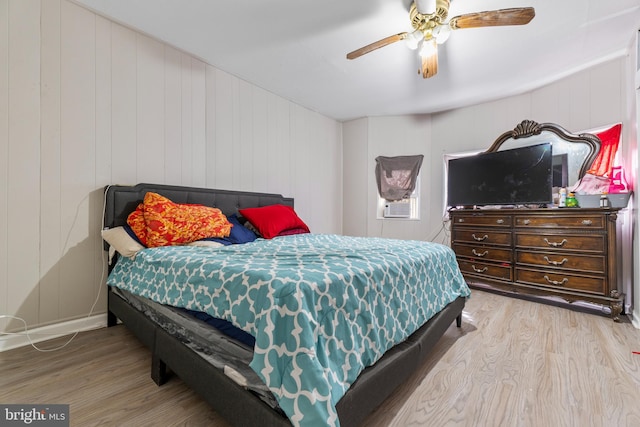 bedroom with light hardwood / wood-style floors, ceiling fan, and wood walls