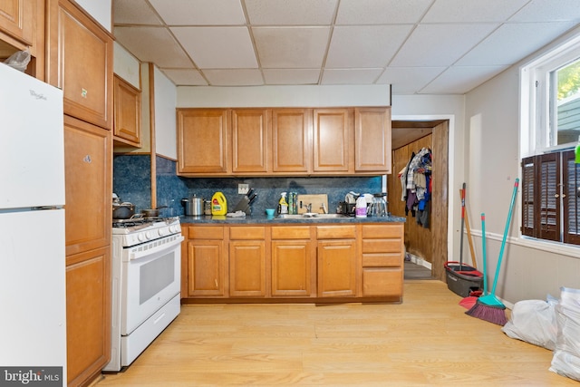 kitchen featuring light wood-type flooring, tasteful backsplash, a paneled ceiling, white appliances, and sink