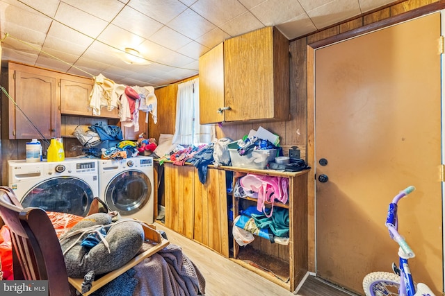 clothes washing area with independent washer and dryer, wood walls, hardwood / wood-style flooring, and cabinets