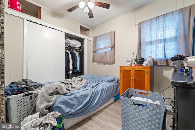 bedroom featuring light wood-type flooring, a closet, wood walls, and ceiling fan