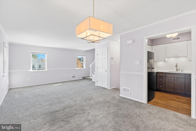 unfurnished living room with sink, crown molding, and light colored carpet