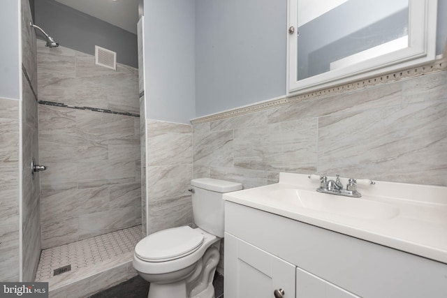 bathroom featuring toilet, vanity, tile walls, and tiled shower