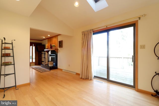 living room with vaulted ceiling with skylight, baseboard heating, and light hardwood / wood-style flooring