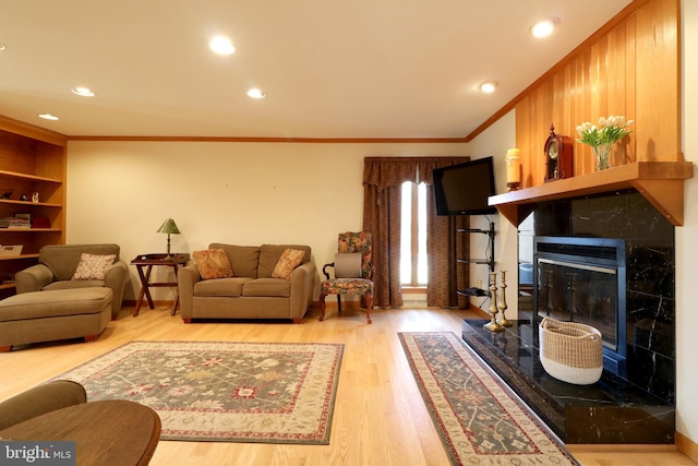 living room with a premium fireplace, wood-type flooring, crown molding, and built in shelves