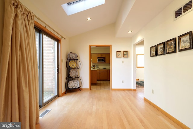 hallway with plenty of natural light, lofted ceiling with skylight, and light hardwood / wood-style floors