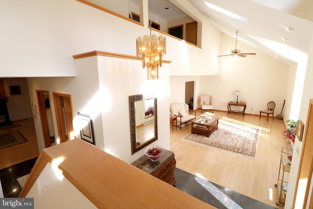 interior space featuring hardwood / wood-style flooring, a skylight, high vaulted ceiling, and ceiling fan with notable chandelier