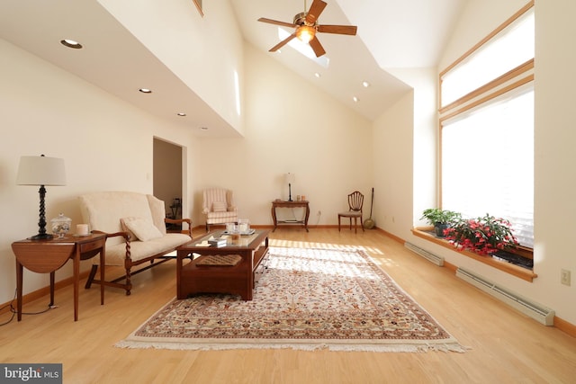 sitting room with baseboard heating, a towering ceiling, ceiling fan, and light wood-type flooring