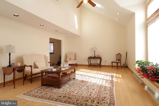 sitting room featuring ceiling fan, a skylight, high vaulted ceiling, light hardwood / wood-style floors, and a baseboard radiator