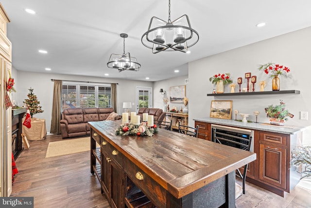 kitchen featuring light wood-type flooring, light stone counters, a kitchen island, a notable chandelier, and wine cooler