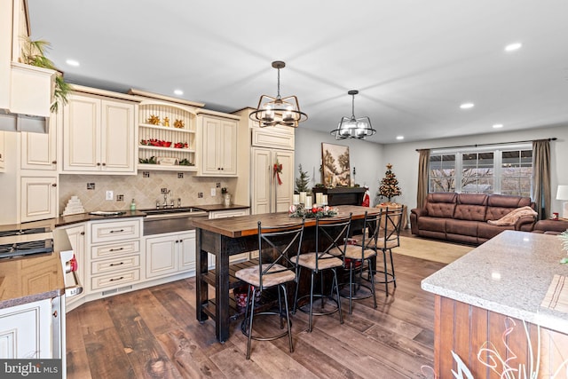 kitchen with dark wood-type flooring, dark stone countertops, a chandelier, pendant lighting, and cream cabinetry