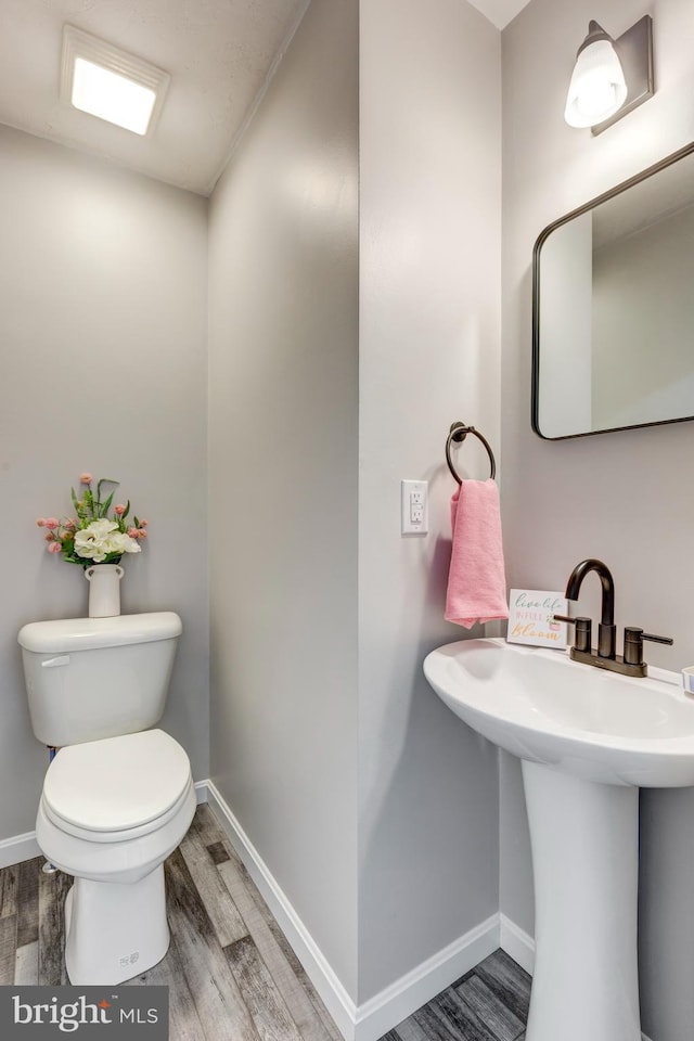 half bathroom featuring baseboards, wood finished floors, a sink, and toilet
