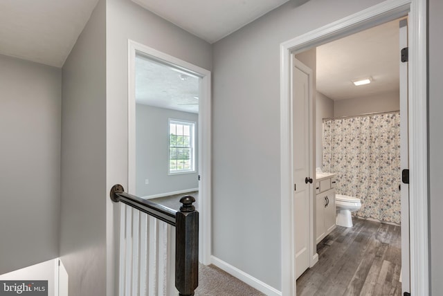 hallway featuring baseboards, an upstairs landing, and dark wood-style flooring